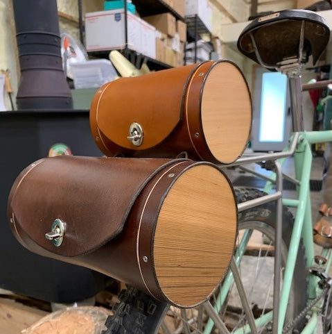 A small honey leather barrel-shaped bicycle saddle bag next to a larger dark brown bag, that's about 50% larger