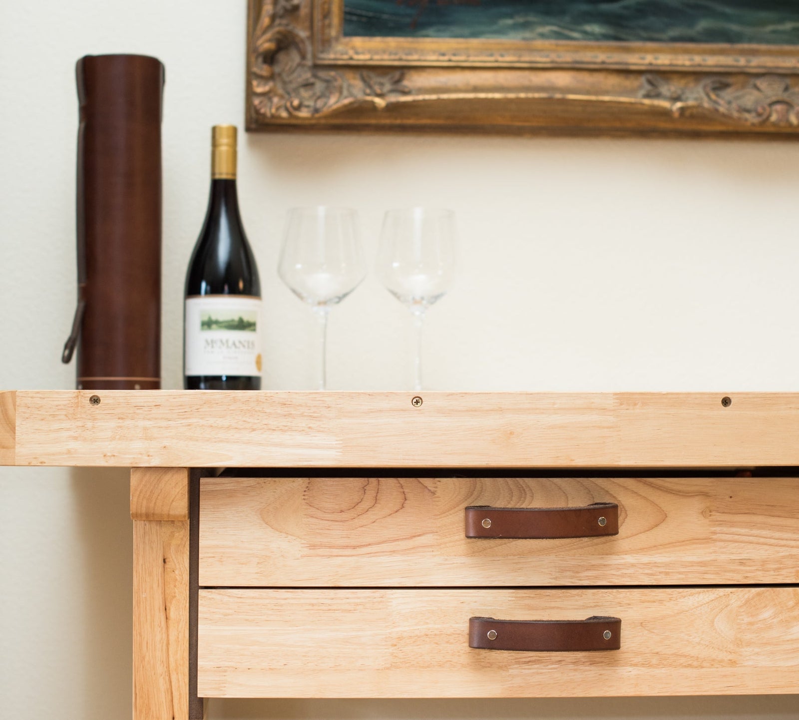 A side table with leather handles, a wine bottle, and a leather wine bottle case