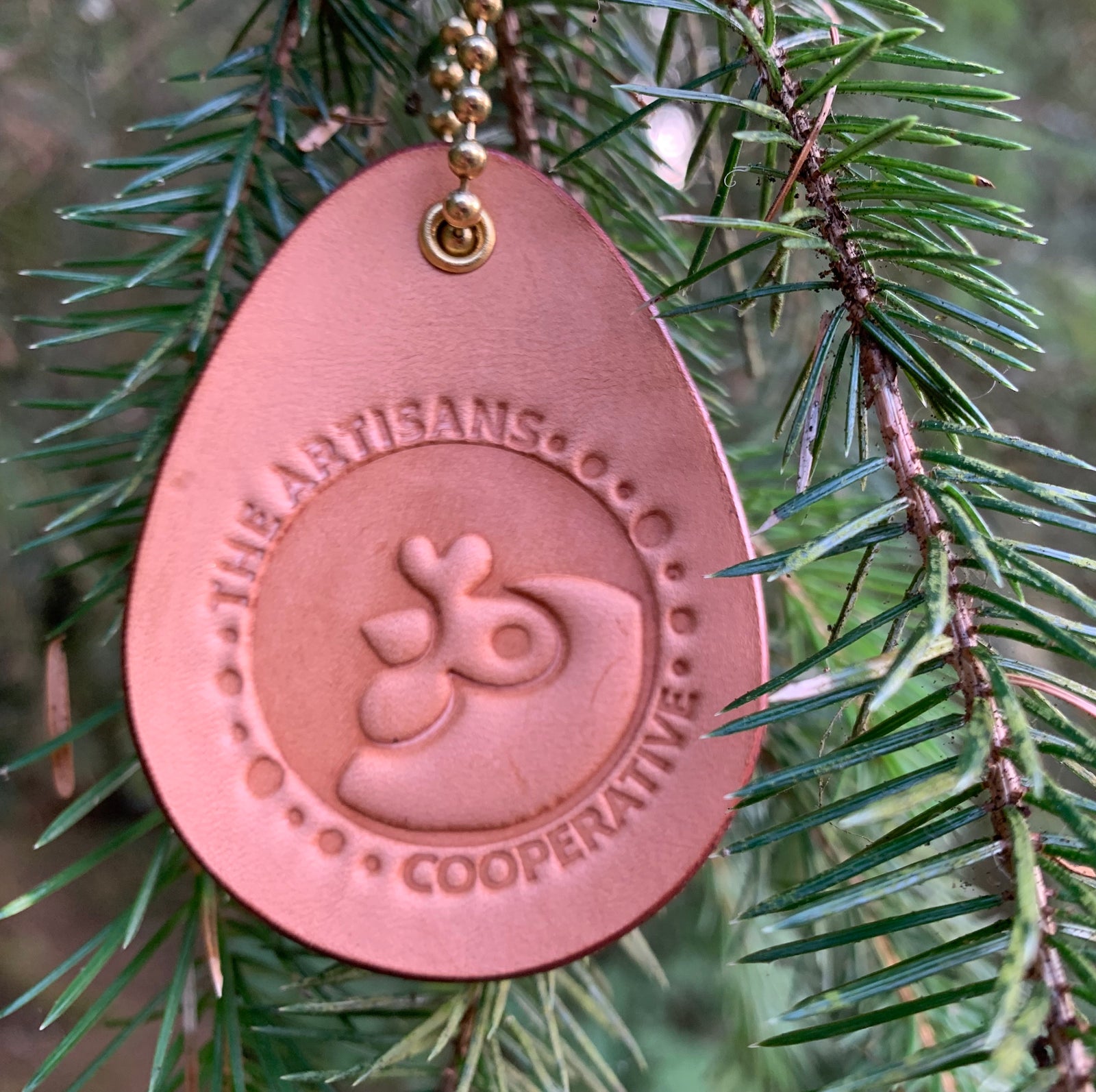Leather keychain with Artisans cooperative logo hanging from a Christmas tree