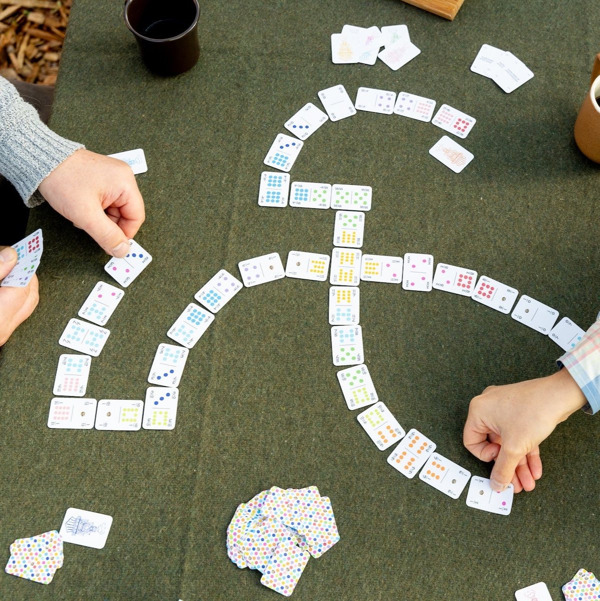 Two people laying down small travel dominoes on a green felt table