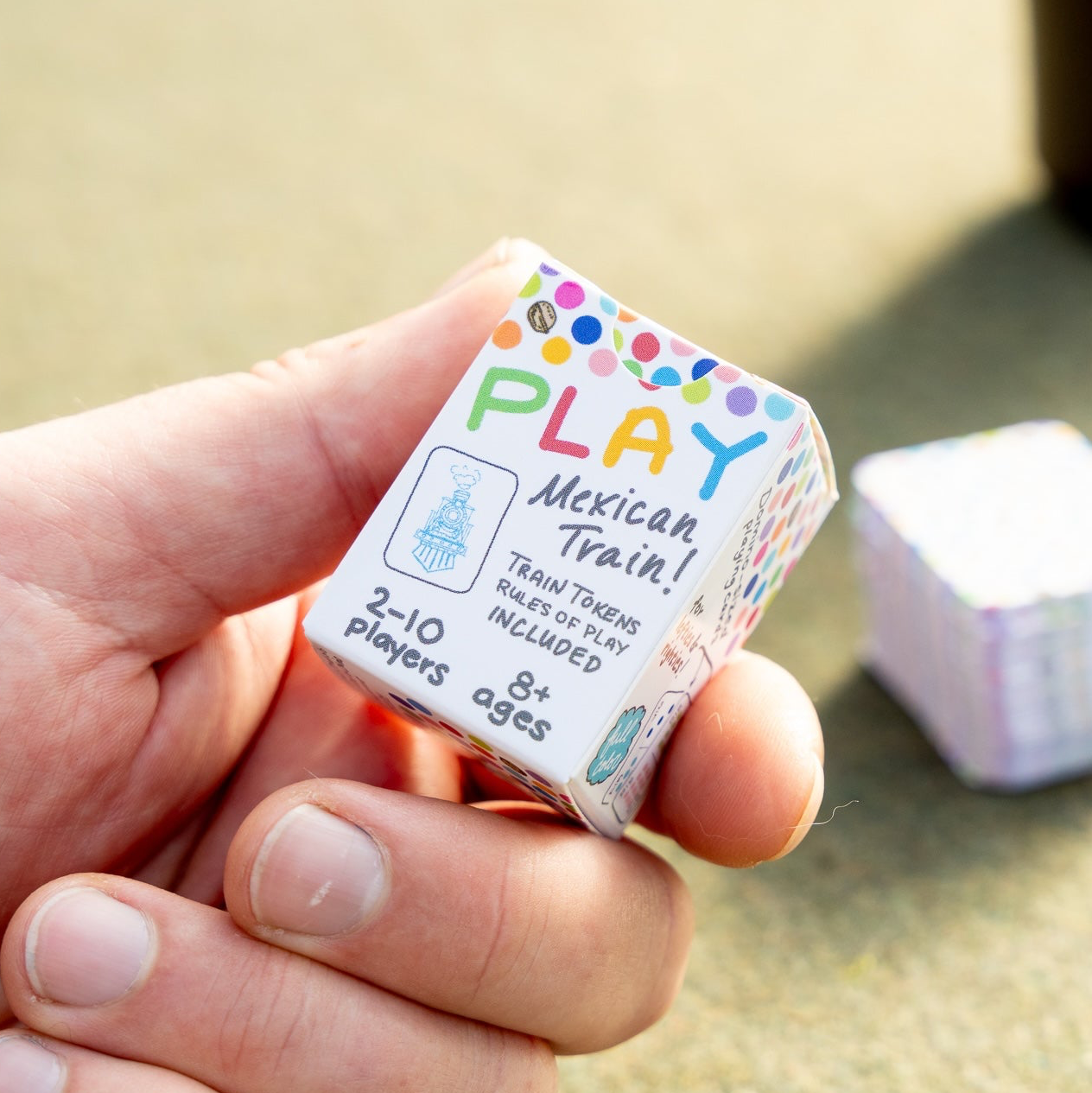 Close-up of a hand holding a box of colorful hand-drawn travel domino playing cards