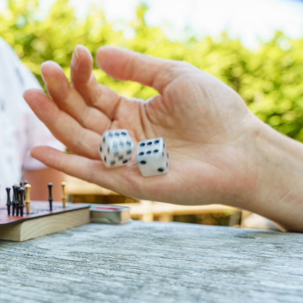 A hand rolling white dice in front of a travel backgammon board outside on a sunny day