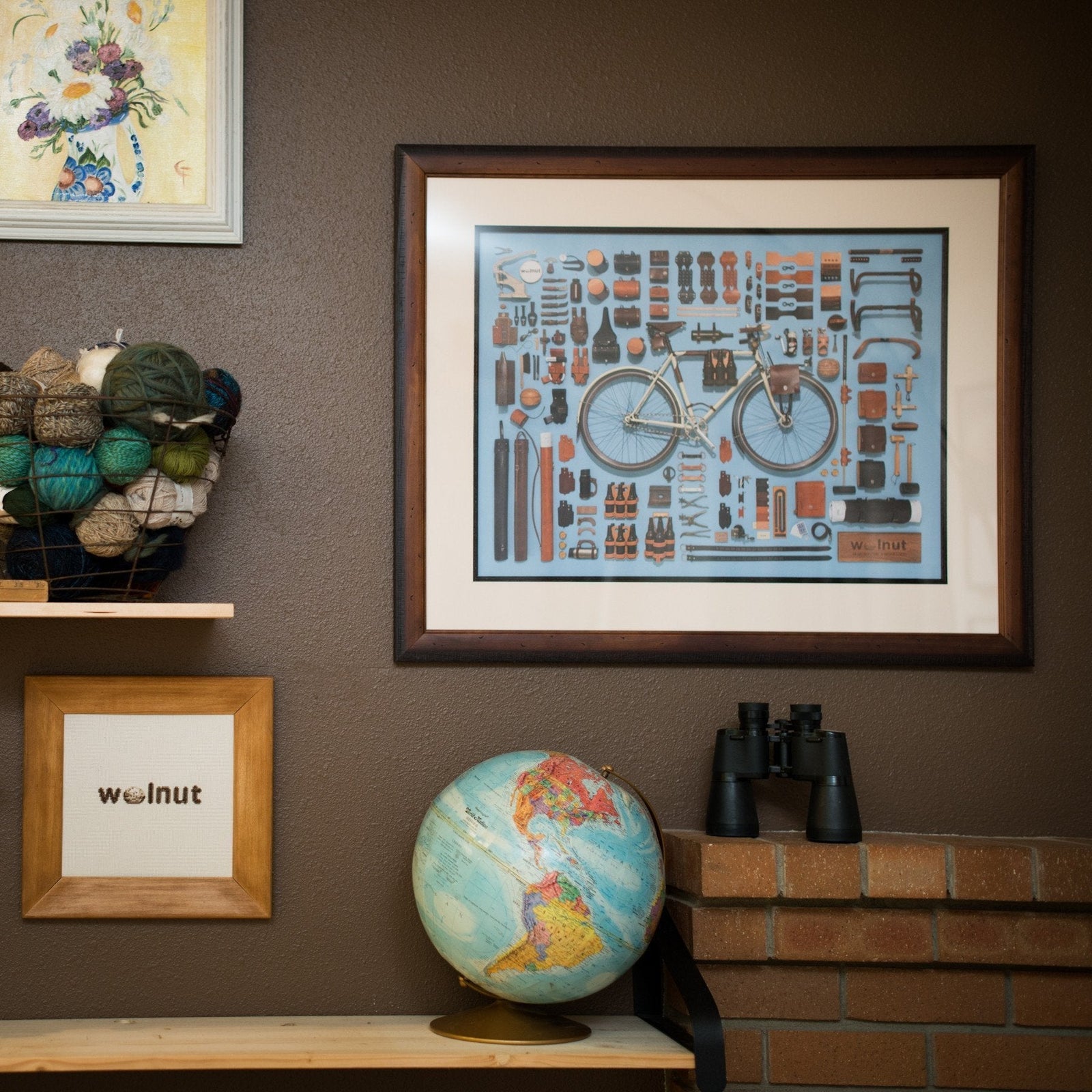 A bicycle-themed poster by Jim Golden featuring the Walnut Studiolo design collection framed nicely on a dark brown wall with a Walnut brand cross-stitch