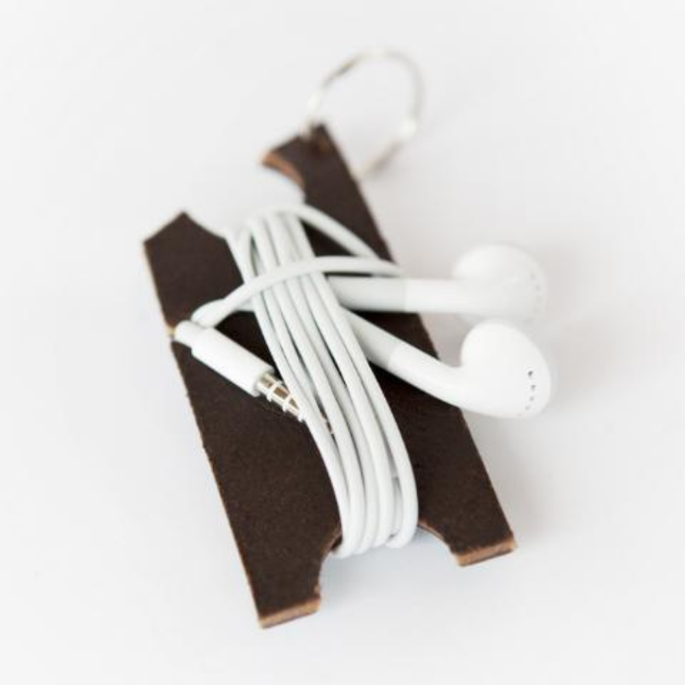 A specially-shaped dark brown leather keychain with a set of earbud cords wrapped around it and tucked into the notches, on a white background