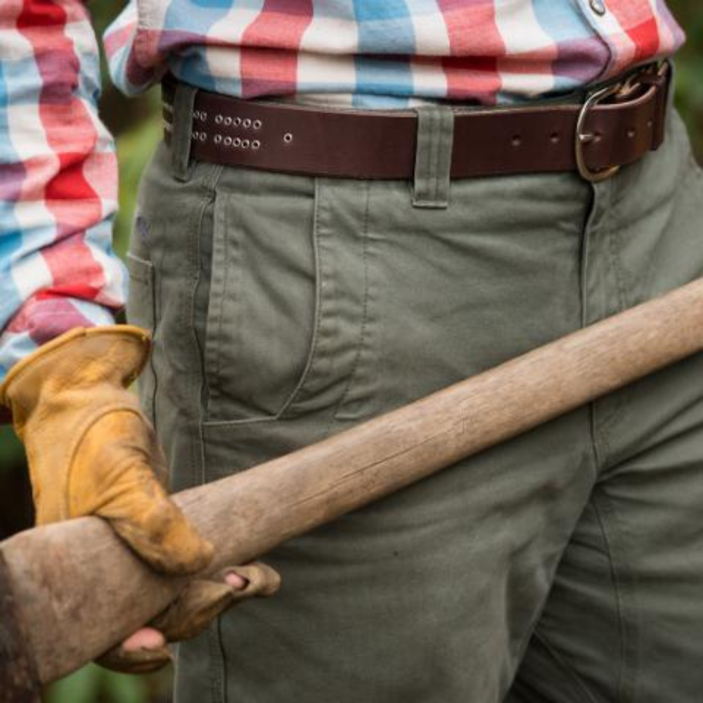 A man in a plaid shirt and canvas pants wearing leather gloves and holding an axe, wearing a dark brown leather handmade cribbage board belt
