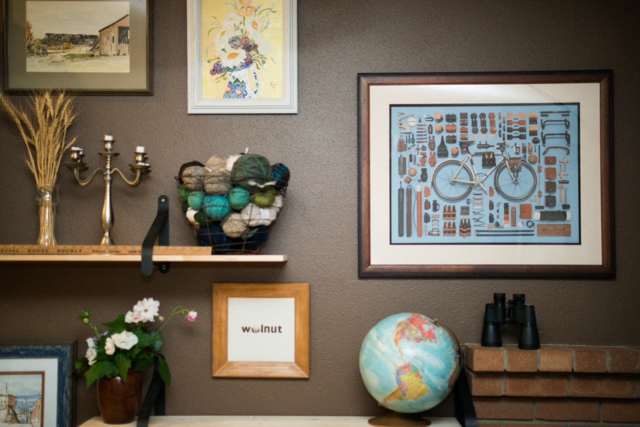 Decorative wall with framed bicycle poster artwork, a globe, a cross-stitch with the Walnut Studiolo logo,and other decorative items.