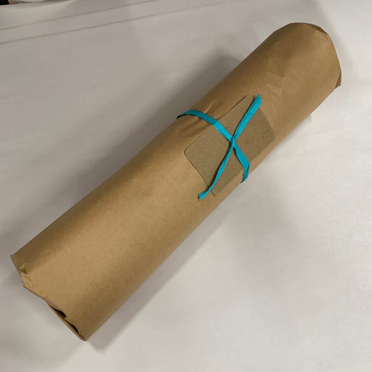 A gift wrapped in a plain brown kraft paper with a turquoise paper raffia ribbon and kraft gift note card