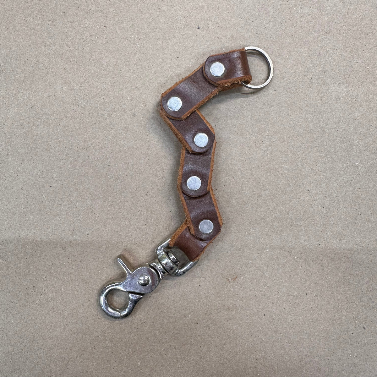 Brown leather keychain with metal clasp on a beige background