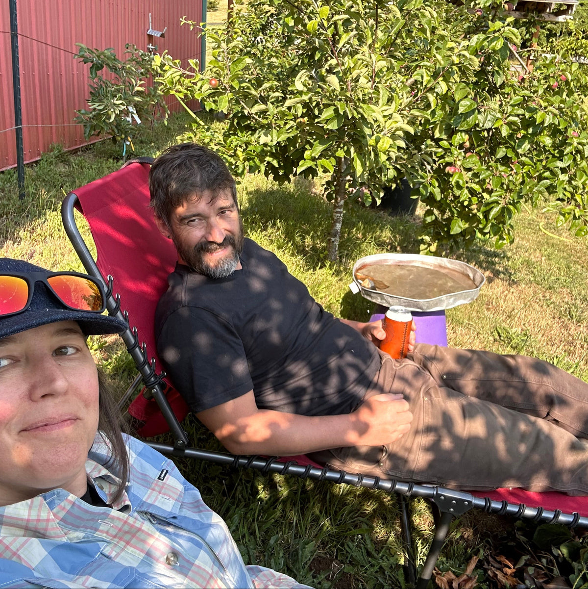Two people in a garden on lounge chairs . The man is holding a can of beer in a brown leather koozie (can sleeve)