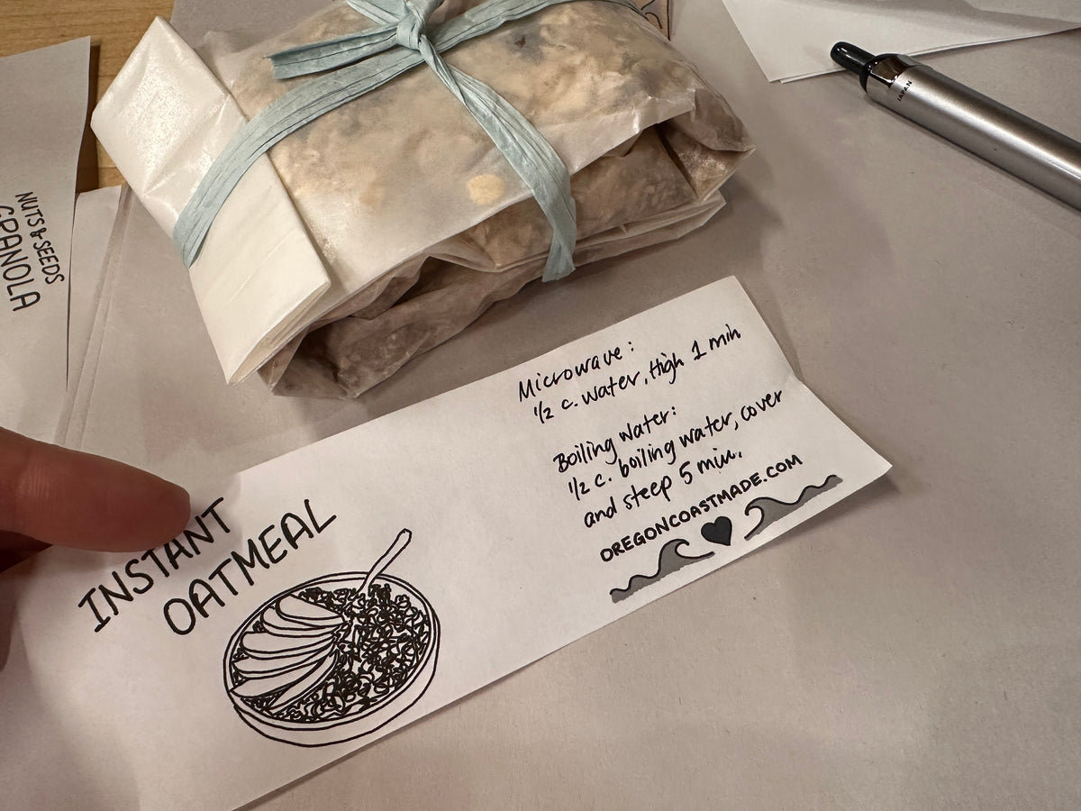 2 paper packets filled with oats tied together with a ribbon, next to a paper packaging label with a drawing that says Instant Oatmeal and instructions for how to cook it in either the microwave or with boiling water
