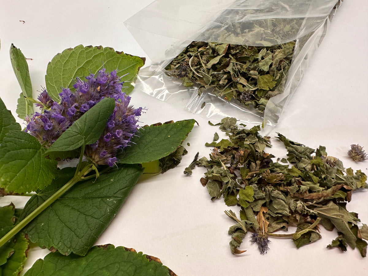 Herbal materials including dried leaves and a purple flower on a white surface.
