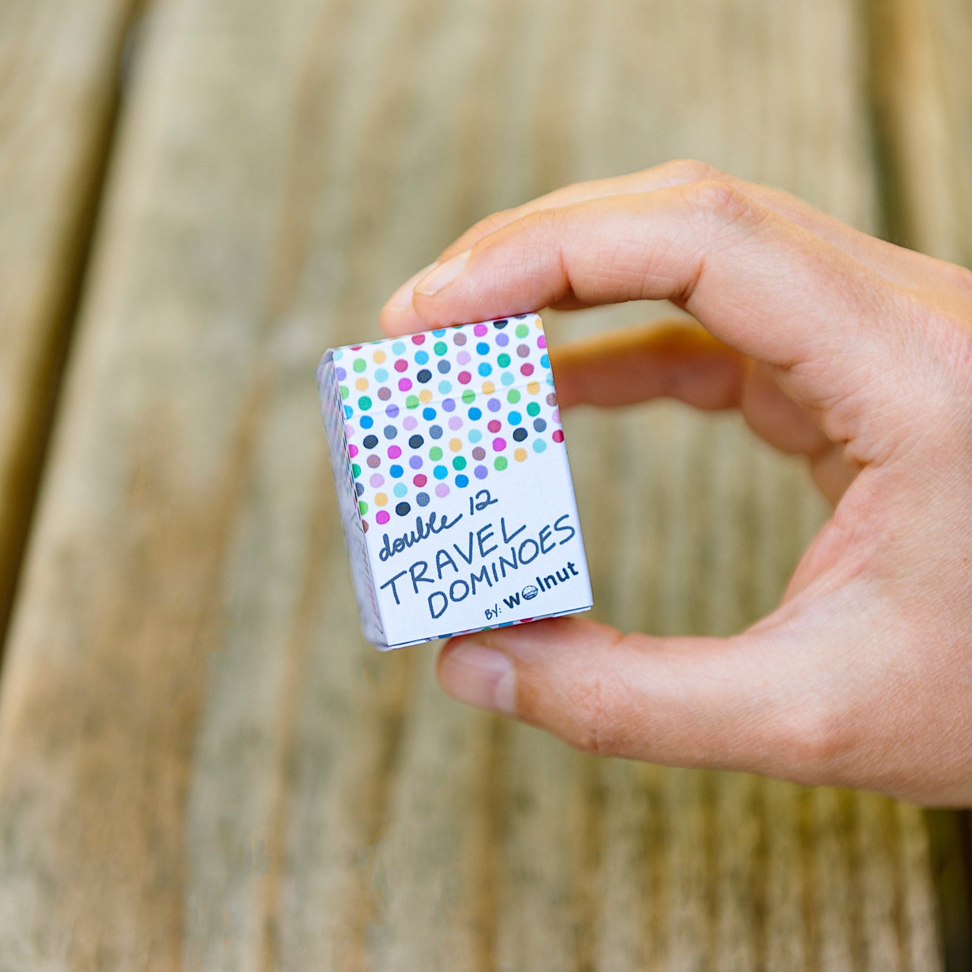 Hand holding domino size cards for scale, pinched inside the palm of the hand, against a picnic table wood backdrop