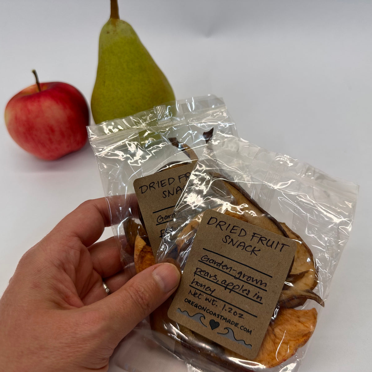 Hand holding a package of dried fruit snacks with an apple and pear in the background.