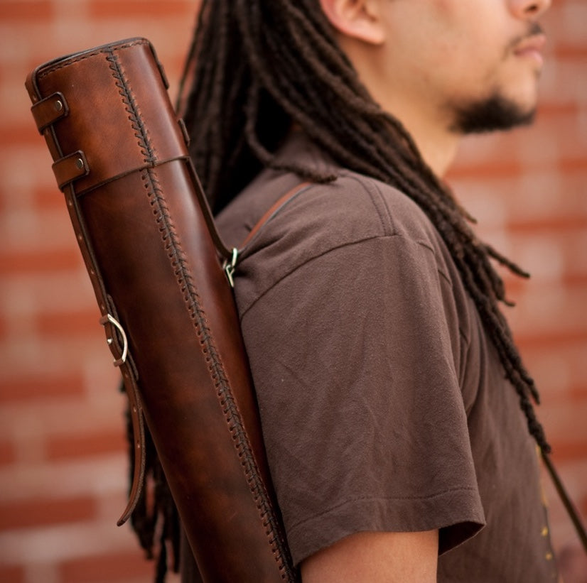 Man wearing a hand-stitched, handcrafted brown leather document tube briefcase on his shoulder against a brick wall 