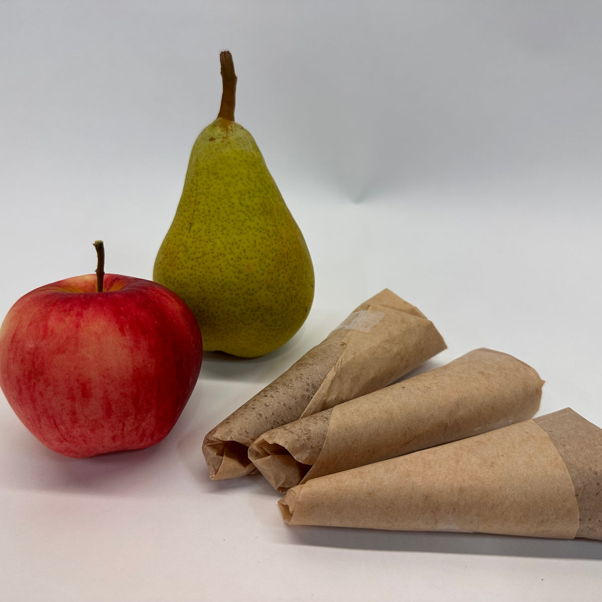 Red apple and green pear with 3 brown deli paper wrapped fruit leather rolls on a white background