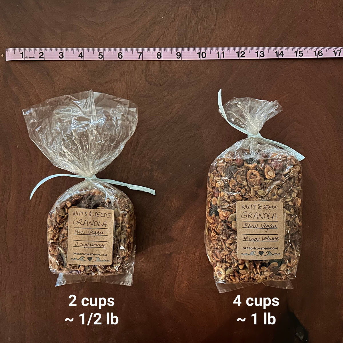 Two packages of granola in different sizes with labeled quantities on a walnut wood surface with a ruler running across the top for scale