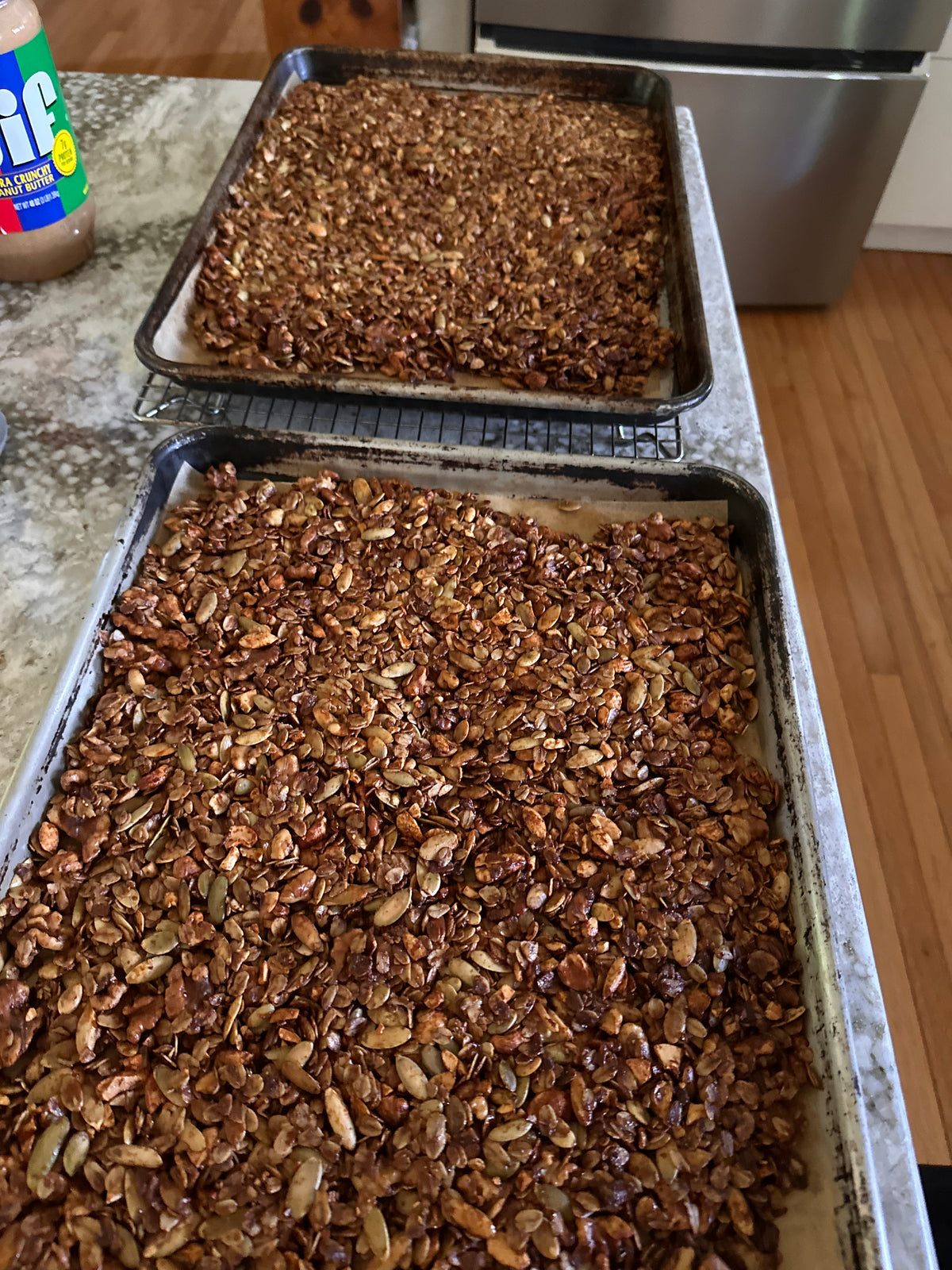 Two sheet trays of crispy browned homemade granola on a kitchen counter