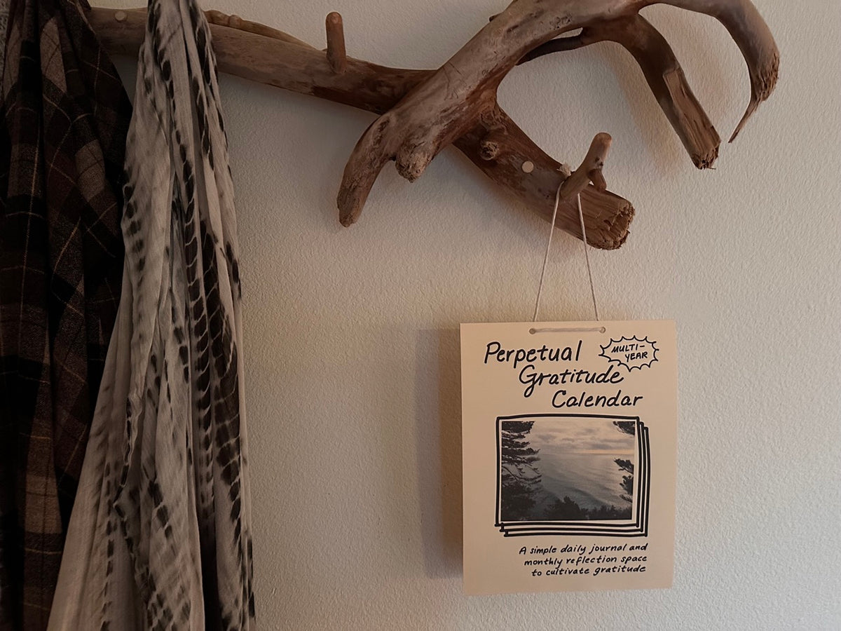 Perpetual Gratitude Calendar hanging on a wall from a handmade driftwood coat rack with cozy textiles hanging