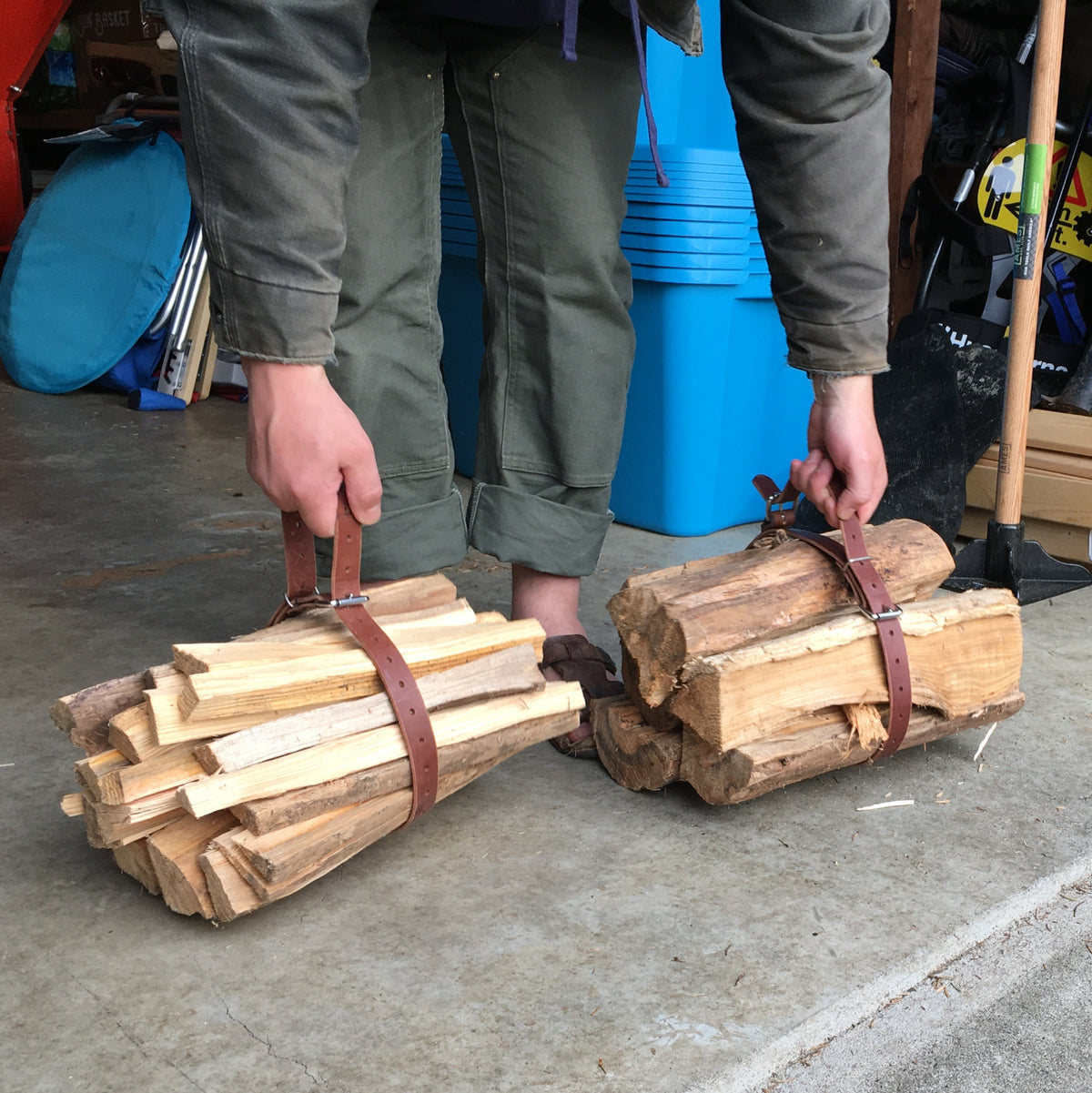 Two bundles of wood tied together with a brown leather belt being lifted by a person in a garage setting.