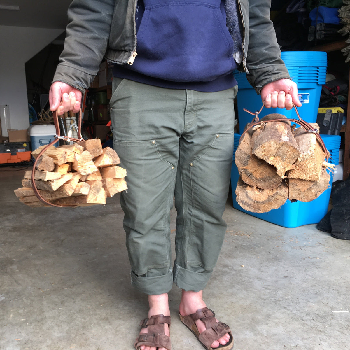 Person carrying two bundles of wood held together with a brown leather belt carrier strap in a garage setting