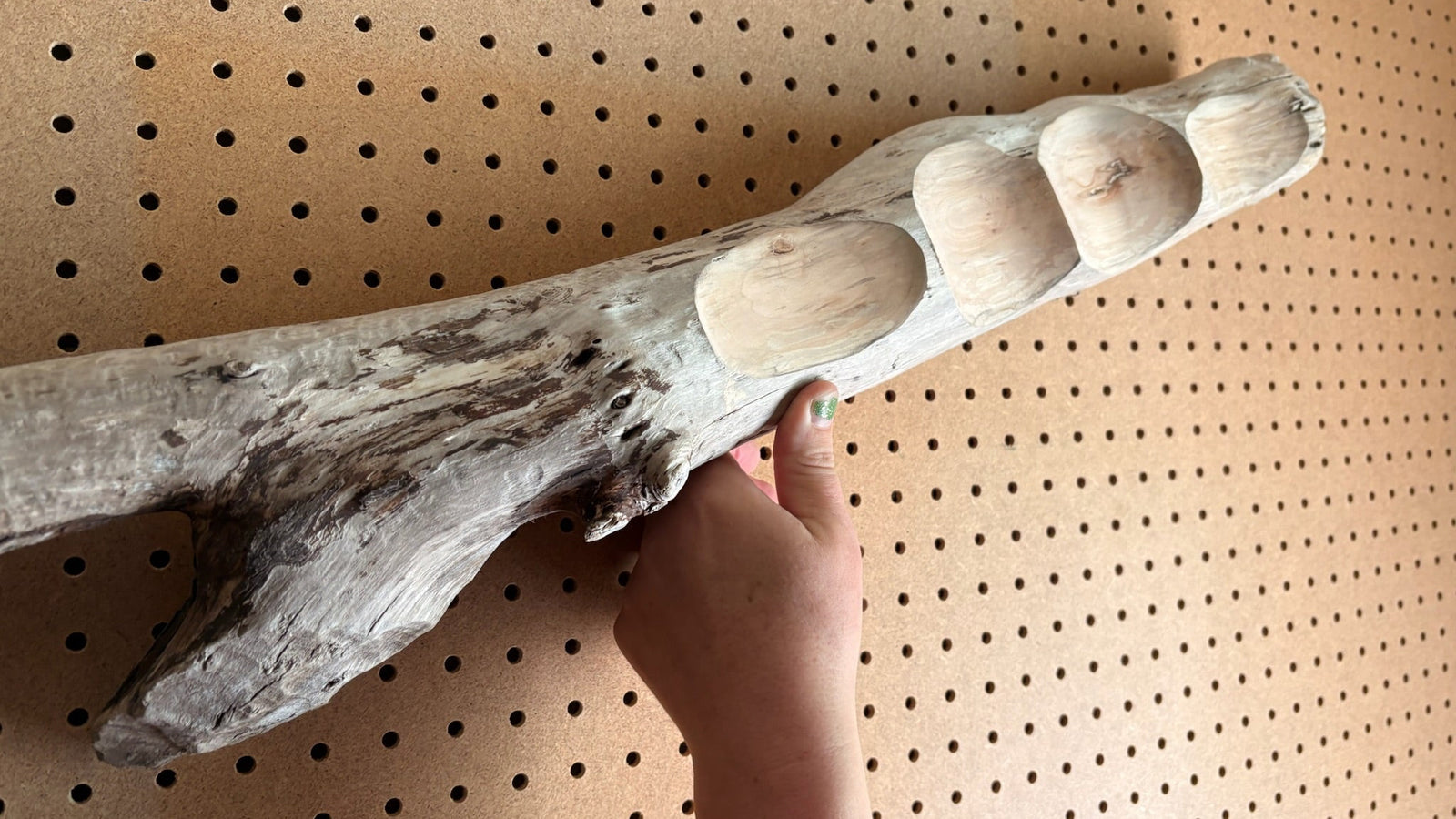 Driftwood with rounded ends held against a pegboard background