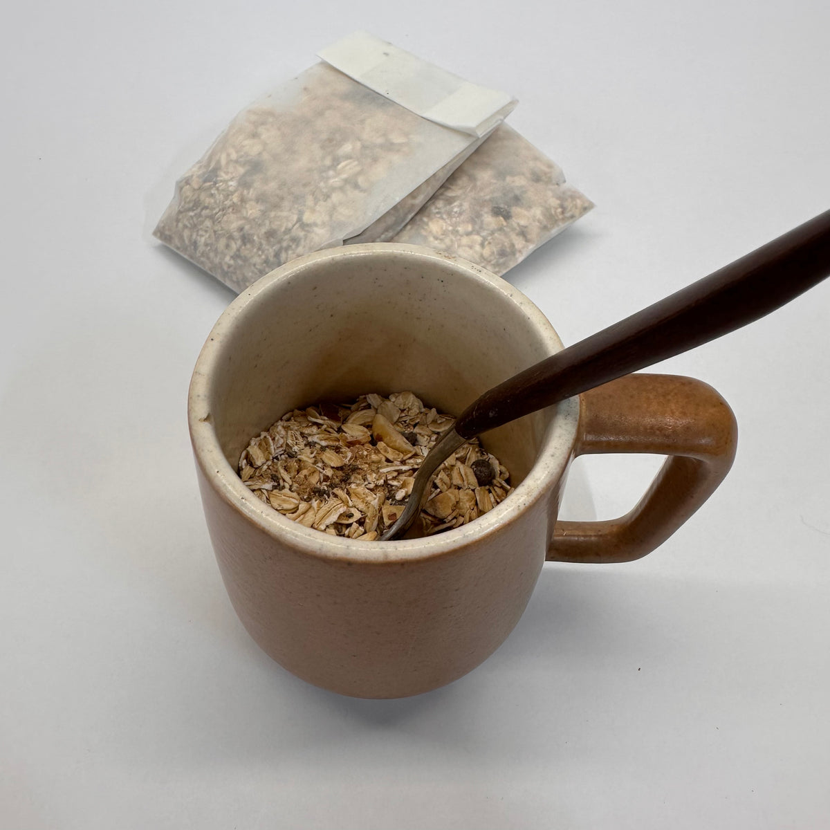 Brown ceramic mug with oatmeal and a spoon, paper oatmeal packets in the background