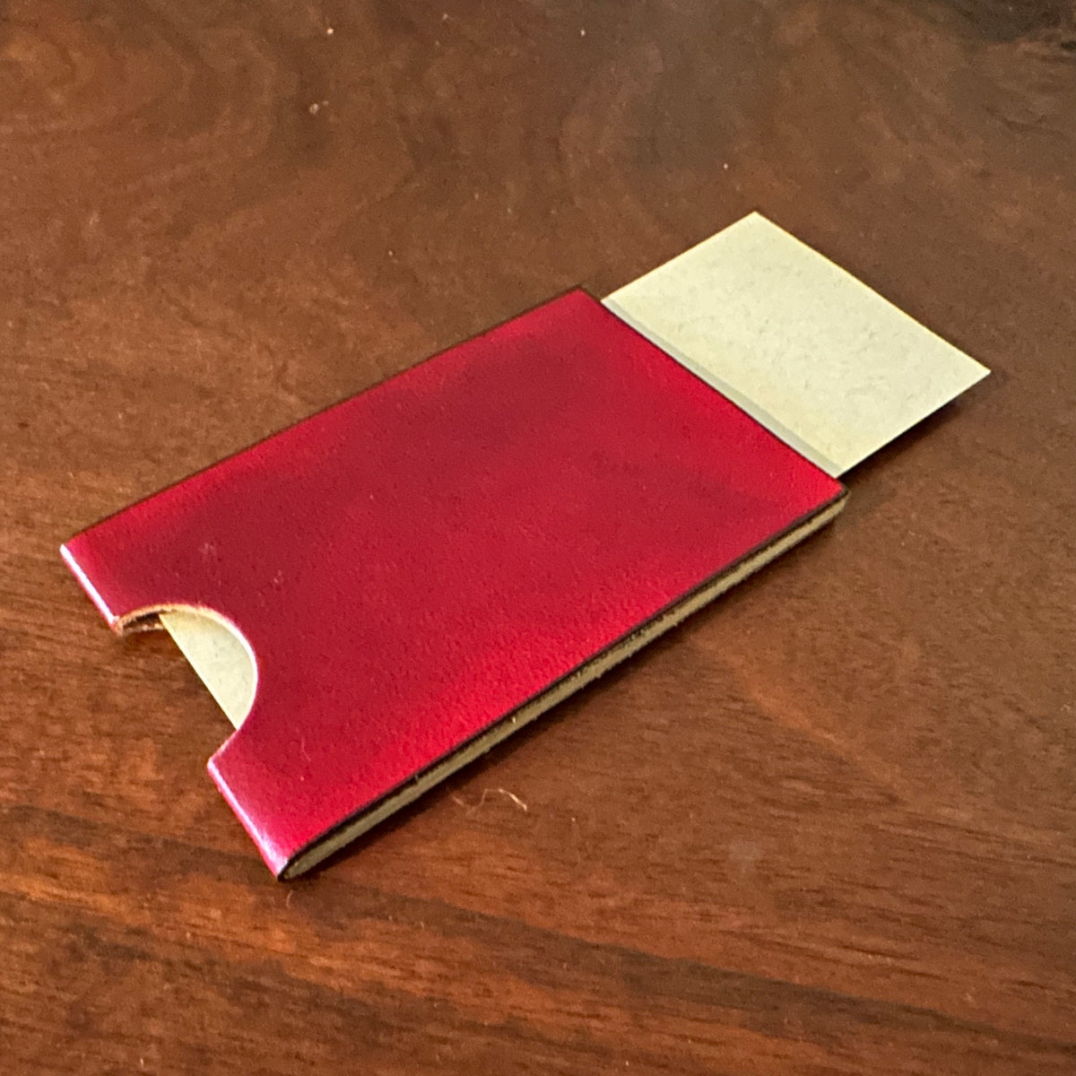 Red leather and walnut wood cardholder on a wooden surface