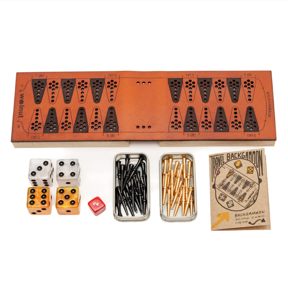 White background photo of a leather travel backgammon board opened up and all the parts to the side: marbleized resin dice, a small red doubling cube, slider tins with brass and black pegs, and a little booklet with score card