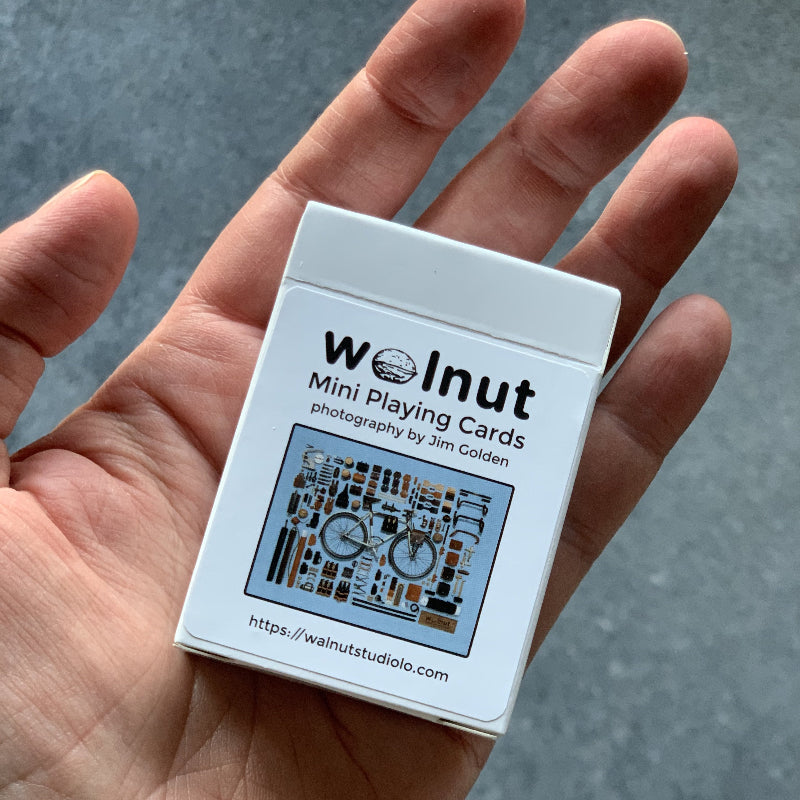 A half-sized deck of playing cards in the palm of a hand, with the label, Walnut Mini Playing Cards, photography by Jim Golden