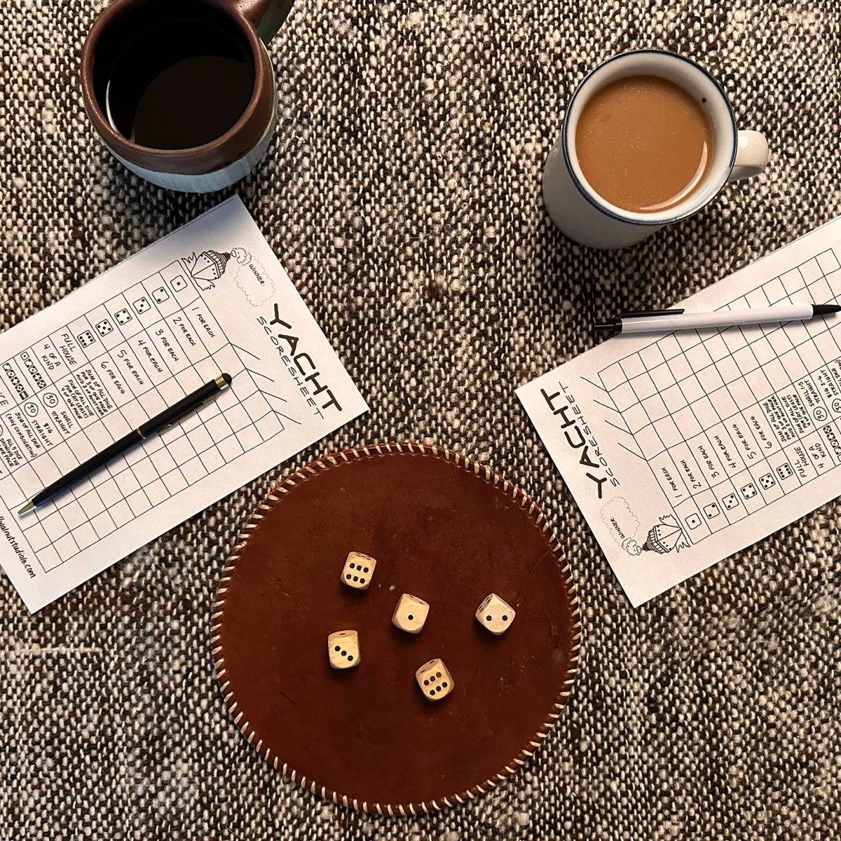 Yacht (Yatzy) game components including dice and score sheets on a textured surface with two coffee cups.