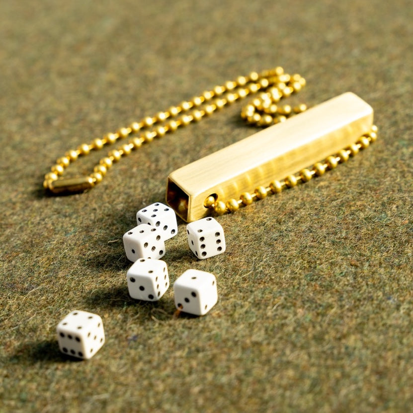 white travel dice in a brass tube with a necklace length beaded ball chain on a green wool army blanket
