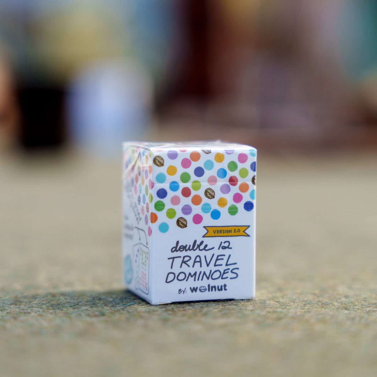 The new Double 12 Travel Domino Playing Card box or carton with the Version 2 badge in yellow, on a table with a blurred-out background