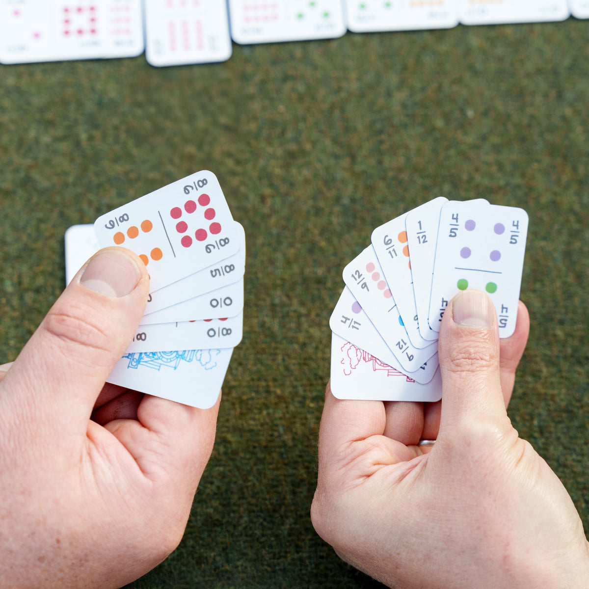 A left-handed person and a right-handed person holding small, travel sized, domino-sized domino playing cards next to each other. There are four corner numbers on each card so the leftie and the right have their cards fanned in different directions but can still see the index numbers. 