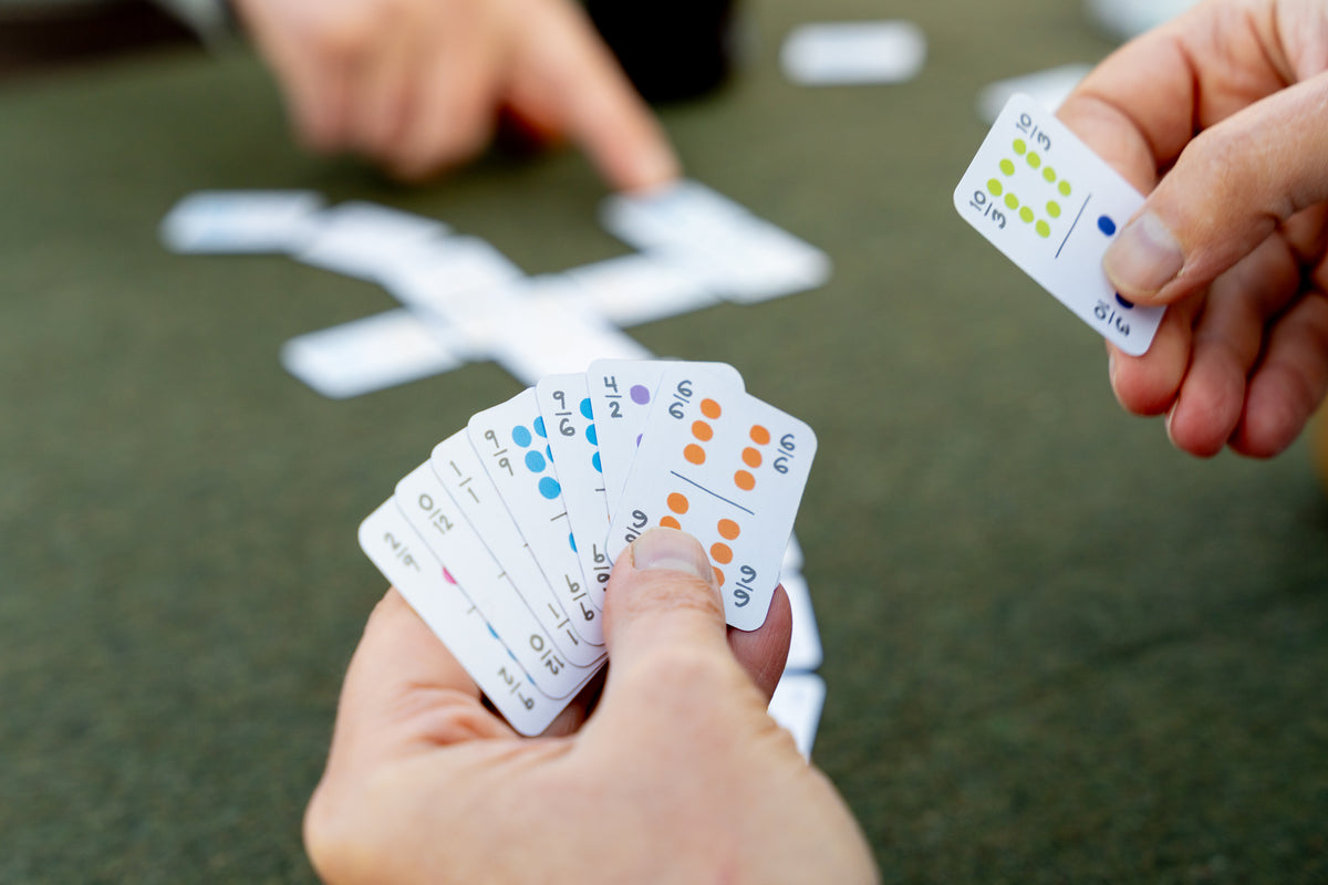 Looking over the shoulder of a person playing Mexican Train domino game using Double 12 domino playing cards. She is holding the cards in her left hand and picking one out with her right to place on the table. 