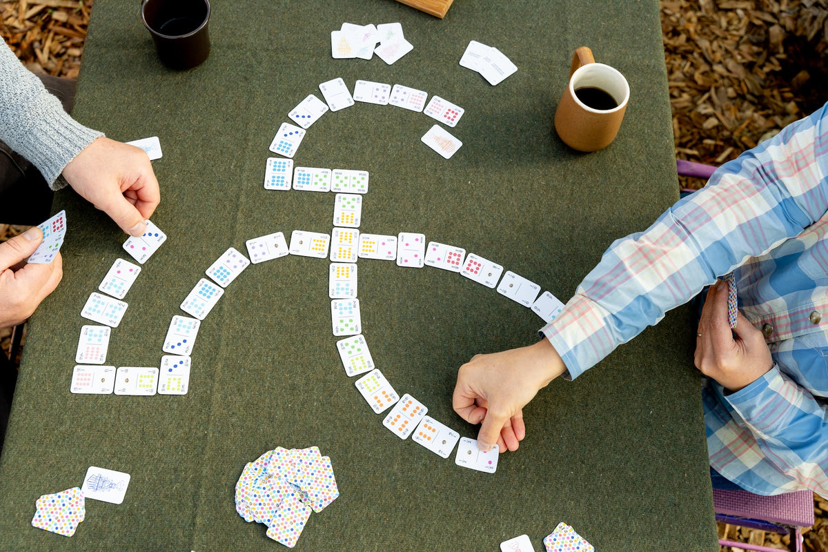 Two people playing a game of dominoes on a green table using playing card dominoes and drinking coffee