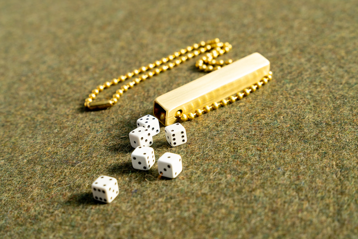 white travel dice in a brass tube with a necklace length beaded ball chain on a green wool army blanket