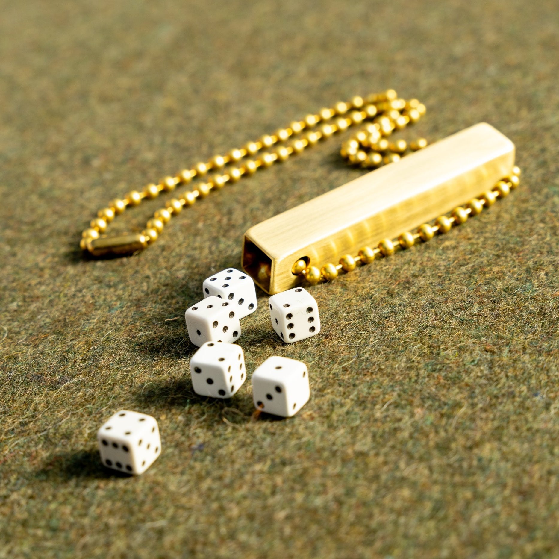 white travel dice in a brass tube with a necklace length beaded ball chain on a green wool army blanket