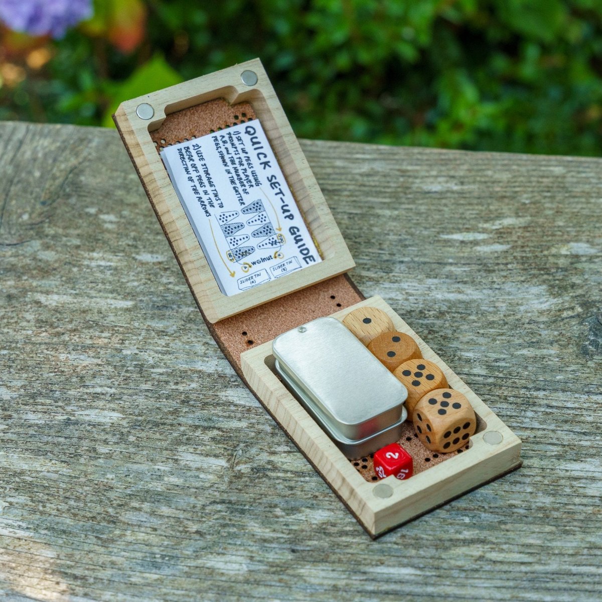 The inside of a folding leather travel cribbage board, showing the leather is undyed on the inside and all the pieces and parts fit inside, and it is closed by four magnets in the corners