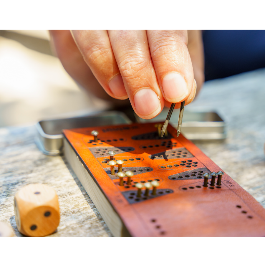 Close-up detail photo of a person&#39;s fingers grasping two brass game pieces from the travel backgammon board and moving two at once. 