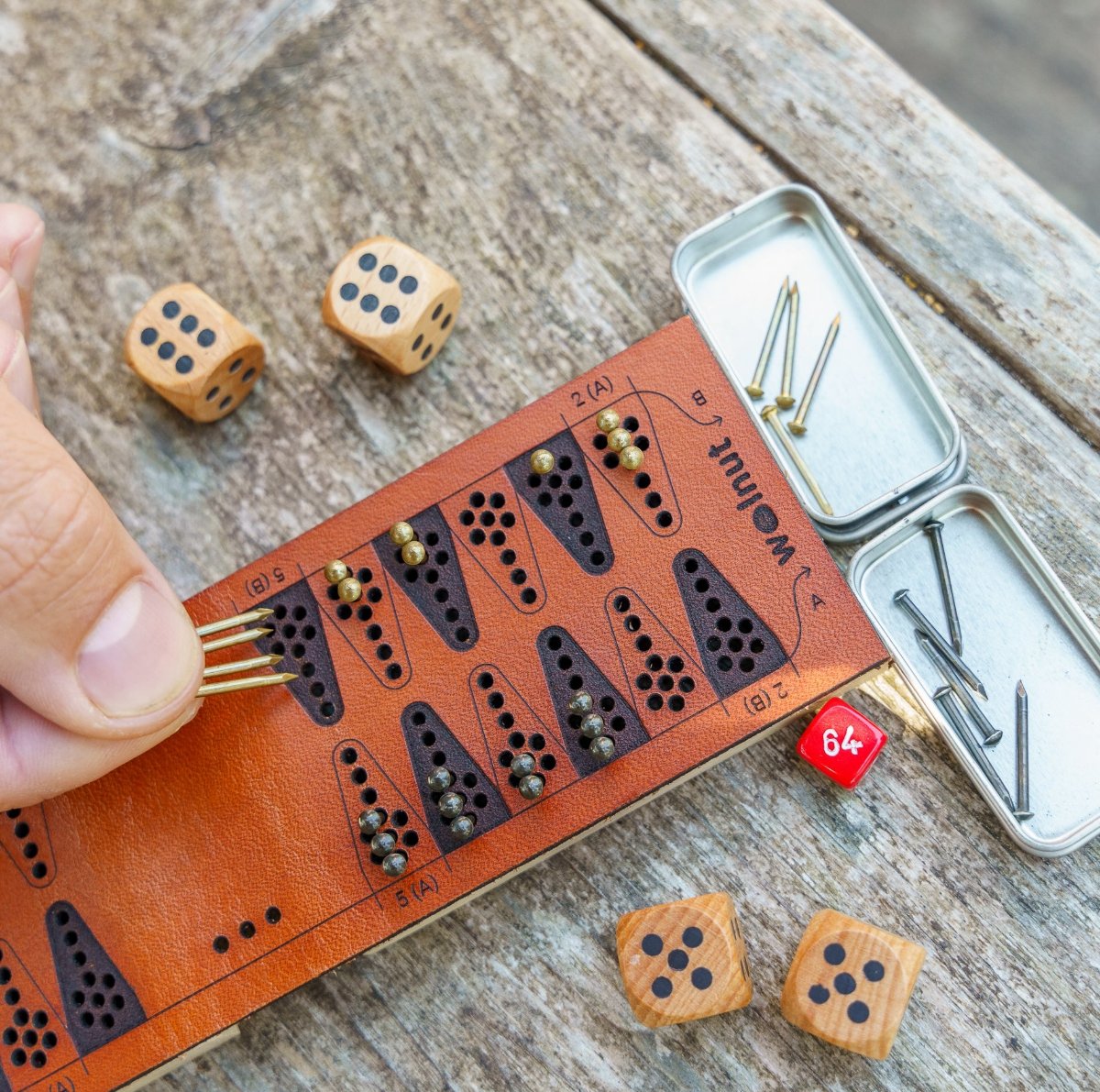 Close-up detail of a leather travel backgammon board laser quality and a man&#39;s hand moving four game pieces (nails) at once because he rolled a double 6 on the dice