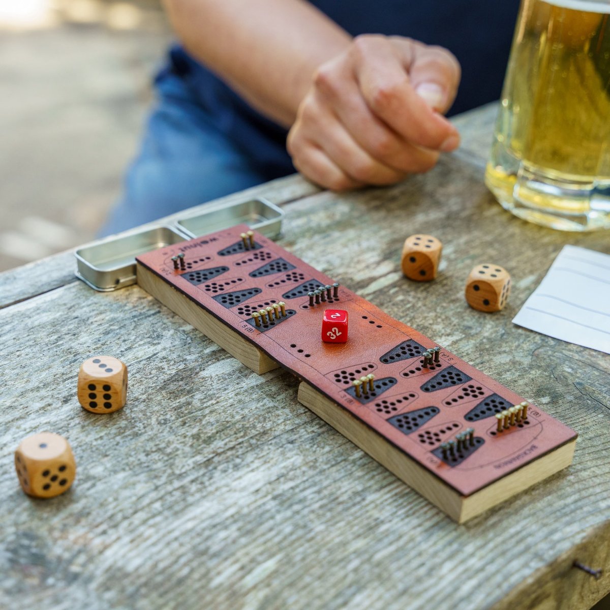 Close-up of a leather travel backgammon travel board opened and set up for play on a picnic bench outdoors. A person&#39;s hand is visible in the background of the photo along with a beer. Fun times! 