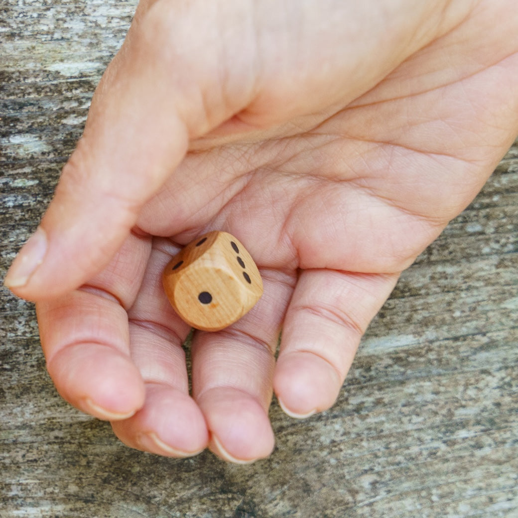 Hand holding a standard 16mm wooden die in the palm of her hand, about to roll on a wooden surface