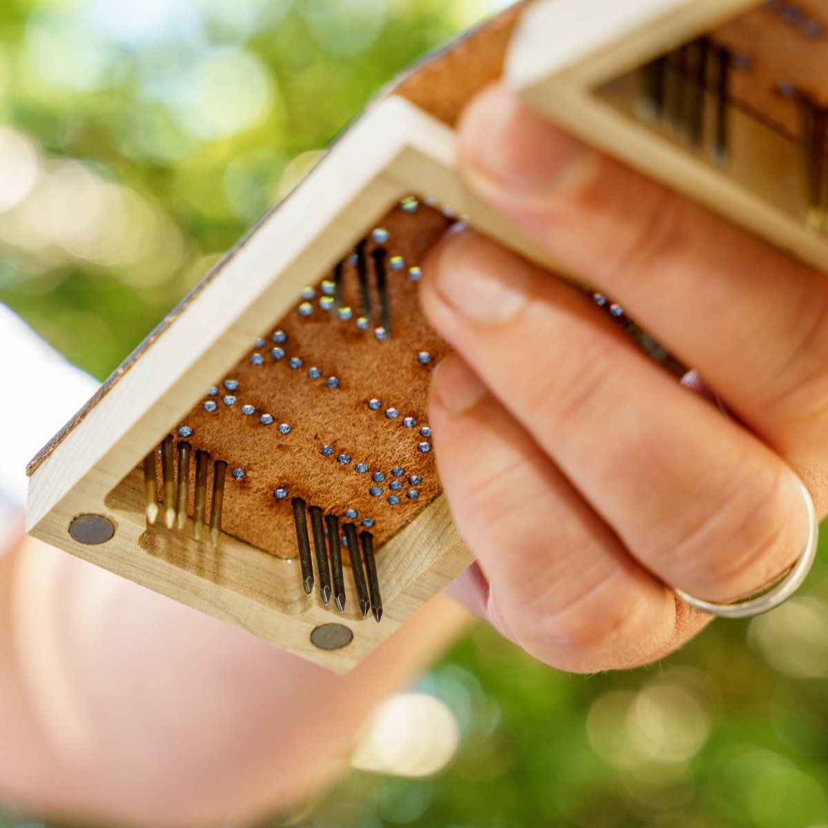 A person&#39;s hand holding up a travel backgammon board with the pegs or game pieces in play but the camera is looking up at the board from the floor so you can see the unfinished leather underneath and that the nail pieces go all the way through the leather, holding secure when moving