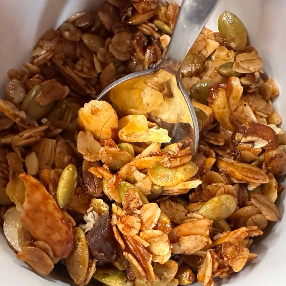 Close-up of a bowl filled with granola and a spoonful being taken out with bright orange pieces and green pepitas