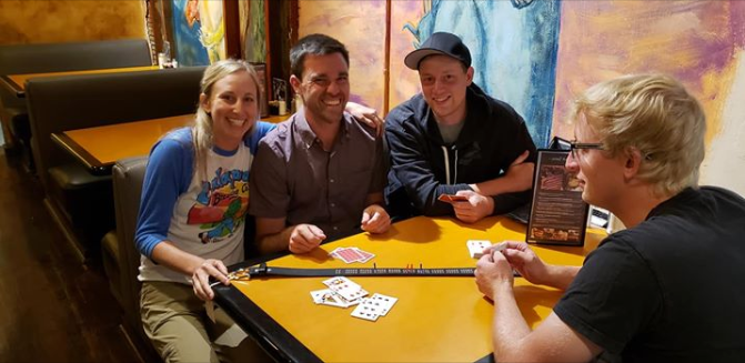 Customer photo of four people sitting at a restaurant table playing cribbage using the cribbage board belt