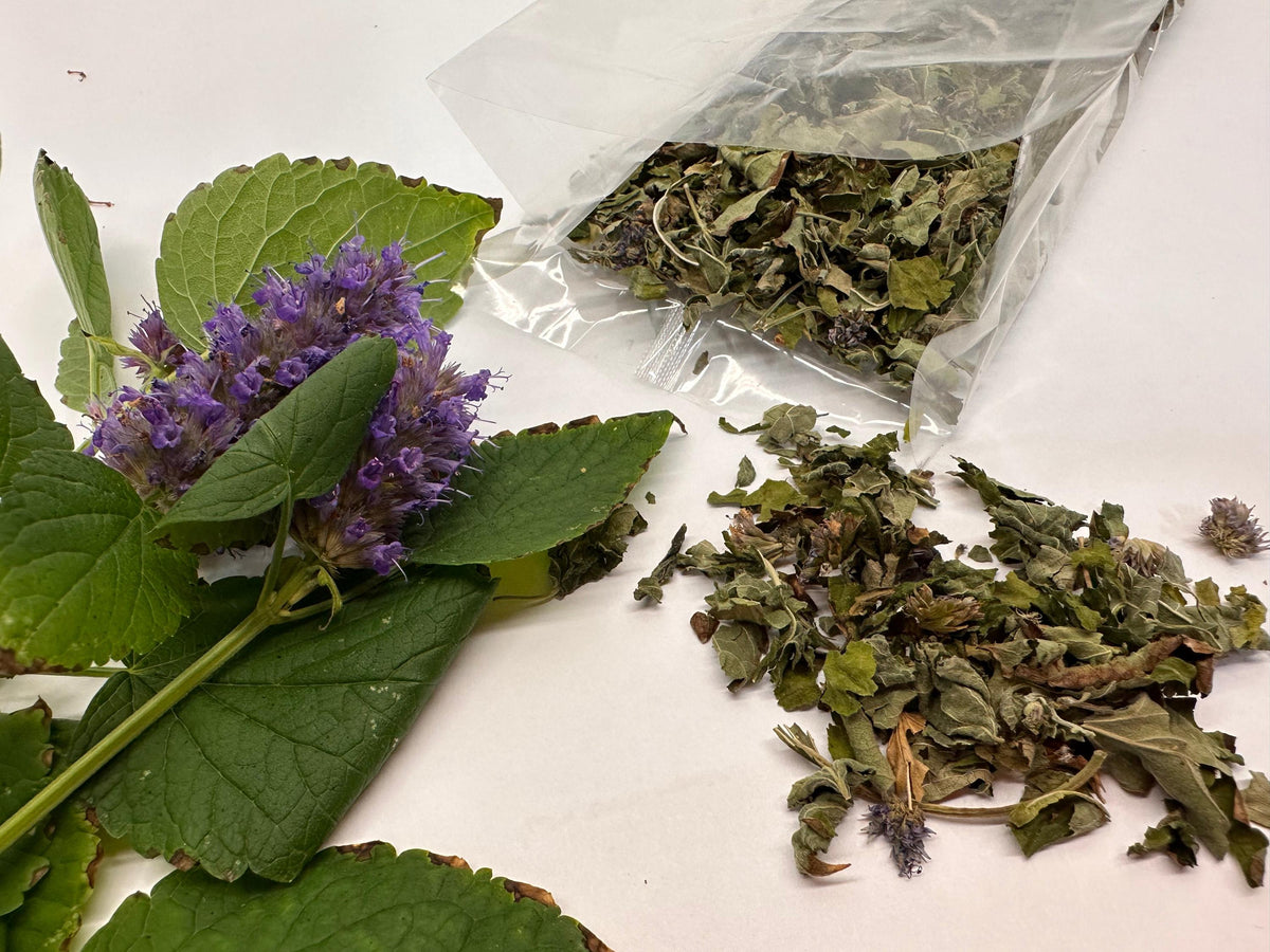 Herbal materials including dried leaves and a purple flower on a white surface.