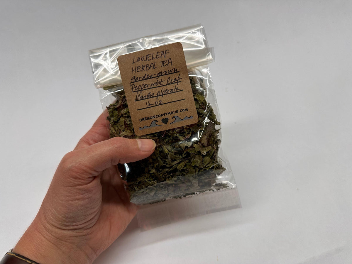 Hand holding a package of dried herbs with a label on a white background