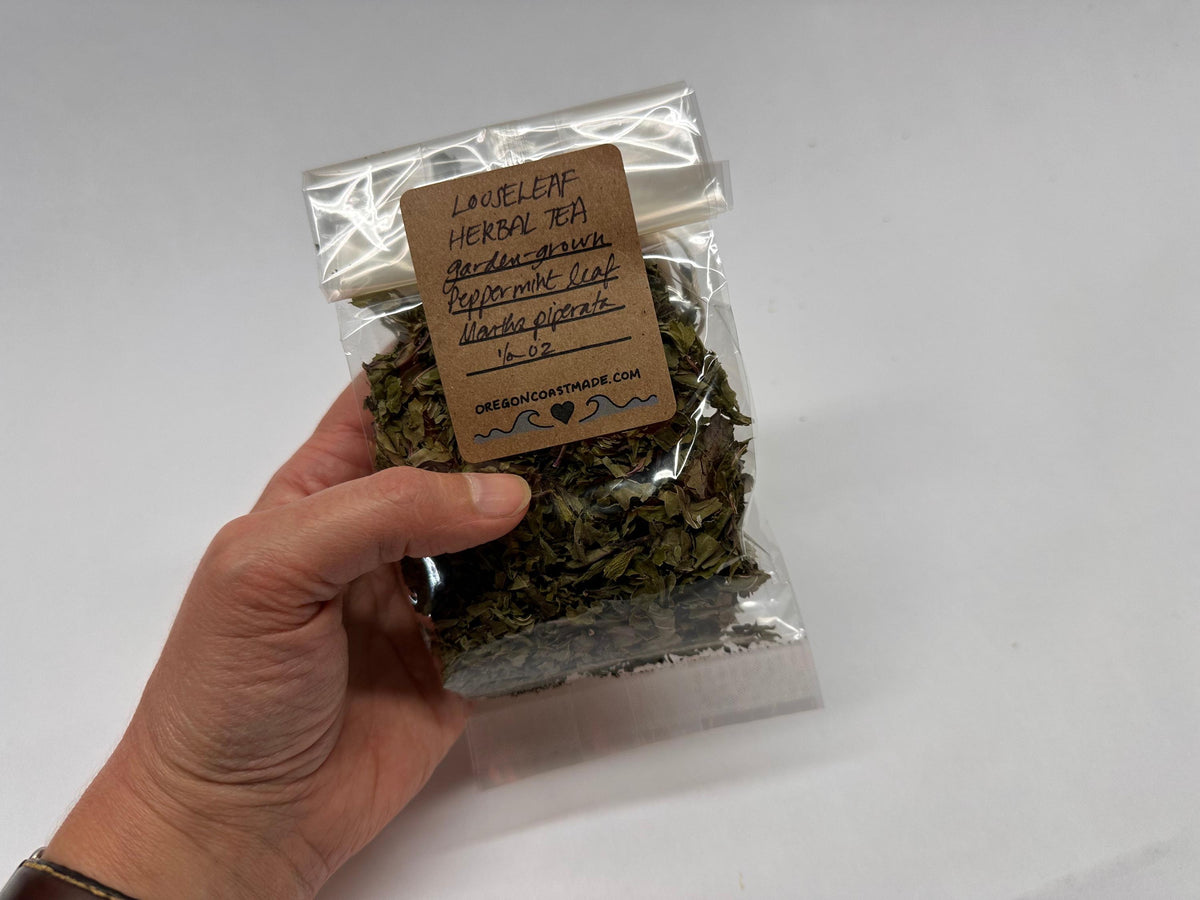 Hand holding a package of dried herbs with a label on a white background