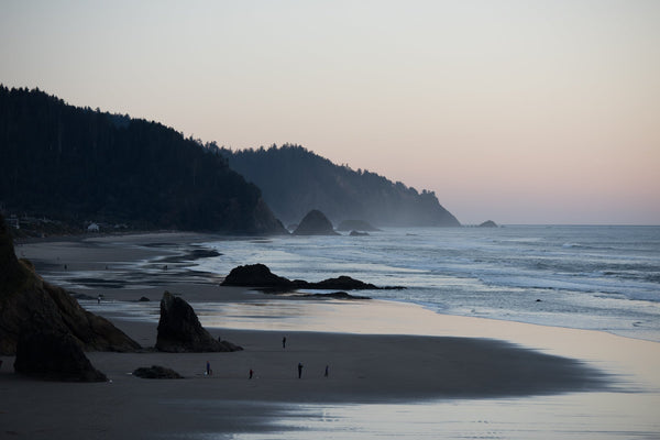 Oregon North Coast Beach scene with people silhouetted against the ocean and cliffs.