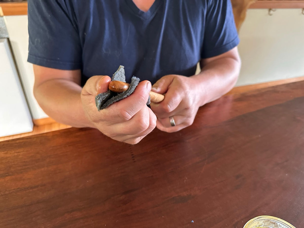 A person's torso seen using both hands to contort an abrasive pad around a wood spoon while sanding